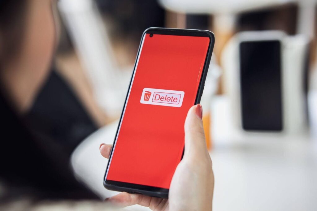 A person holding a smartphone that has a red background with a delete notification, which represents how to remove a phone number from a Discord account.